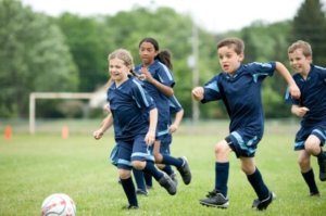 A group of children running around a soccer ball.