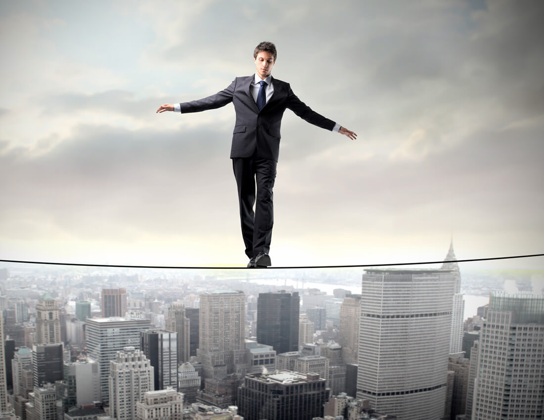 A businessman balancing on a tight rope over a city.
