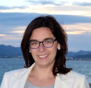 A woman wearing glasses and a blazer in front of the ocean.