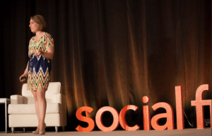 A woman standing on stage in front of a social fx sign.