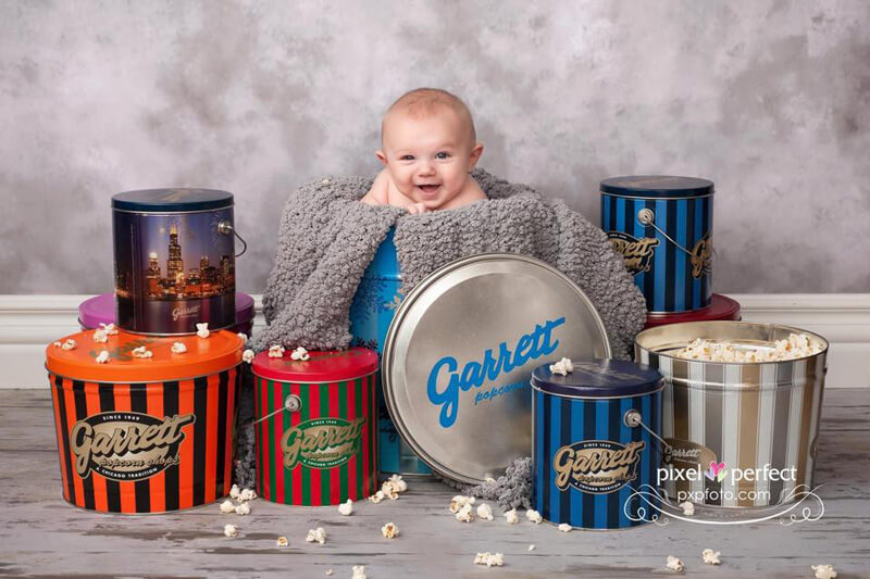 Baby surrounded by Garrett Popcorn tins