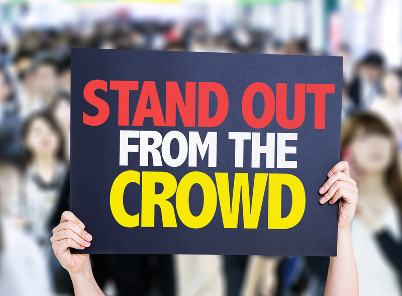A person holding up a sign that says stand out from the crowd.