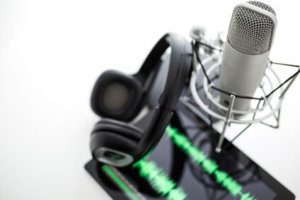 A microphone with headphones and a tablet on a white background.