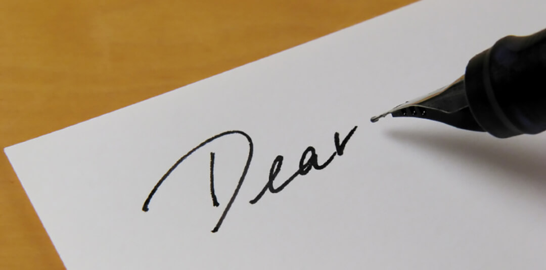 A pen is writing the word dear on a piece of paper.