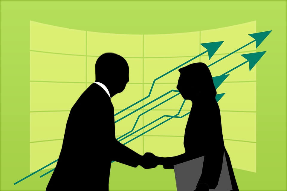 A silhouette of a businessman and woman shaking hands in front of a graph.