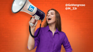 A woman in a purple shirt enthusiastically speaks into a large megaphone branded with the LinkedIn logo, promoting LinkedIn's name pronunciation feature. The background is a vibrant orange brick wall. White text on the upper right corner lists two Twitter handles: @GoVengreso and @M_33Jr.