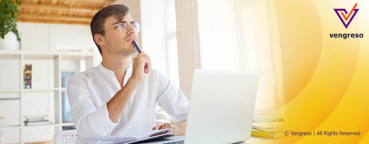 man with glasses thinking sitting in front of a laptop