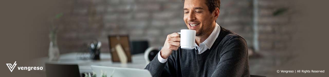 man with a mug smiling in front of a computer