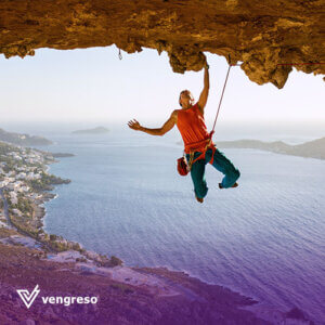 a climber hanging on one hand from a cliff over a big lake