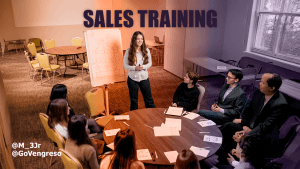 A woman stands near a flip chart, smiling, and leads a sales training session for a group seated around a table with papers and pens. The room is half purple-tinted. "SALES TRAINING" is displayed above, with social media handles "@M_3Jr" and "@GoVengreso" in the corner.