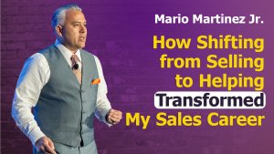 A man in a gray vest and tie stands on stage with a microphone headset. The purple brick wall behind him displays: "Mario Martinez Jr. How Shifting from Selling to Helping Transformed My Sales Career," with "Transformed" highlighted in white.
